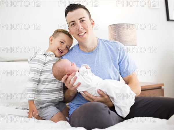 Father carrying daughter (0-1 months) and sitting on bed with son (4-5)