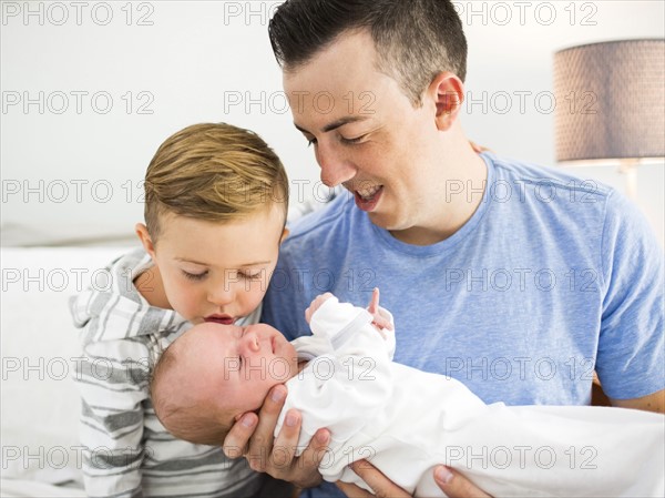 Father carrying daughter (0-1 months) and sitting on bed with son (4-5)