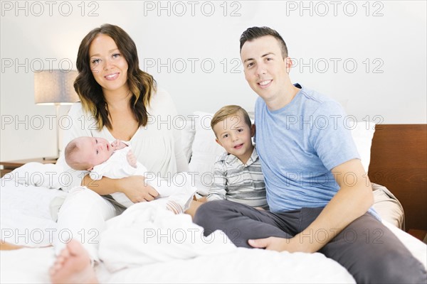Parents sitting with daughter(0-1 months) and son (4-5) on bed in bedroom