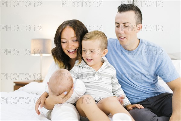 Parents sitting with daughter(0-1 months) and son (4-5) on bed in bedroom