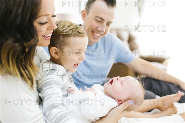 Parents sitting with daughter(0-1 months) and son (4-5) on bed in bedroom