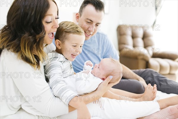 Parents sitting with daughter(0-1 months) and son (4-5) on bed in bedroom