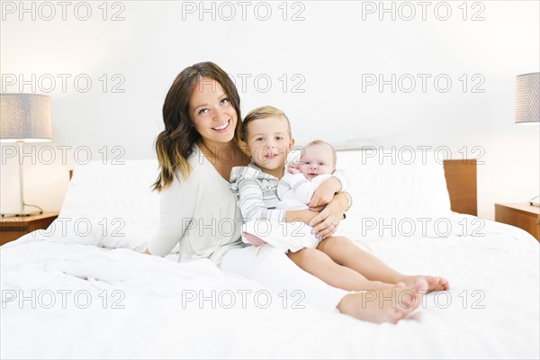 Brother (4-5) carrying sister (0-1 months) and sitting on bed with mother