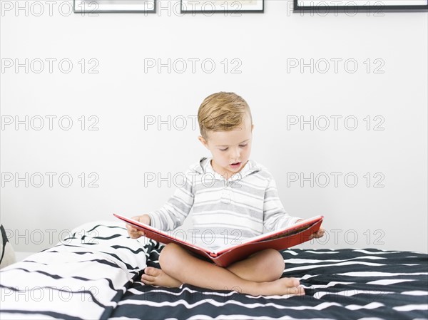 Boy (4-5) sitting on bed and reading book