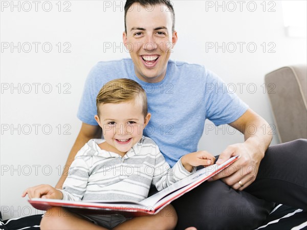 Father and son (4-5) sitting on bed and holding book