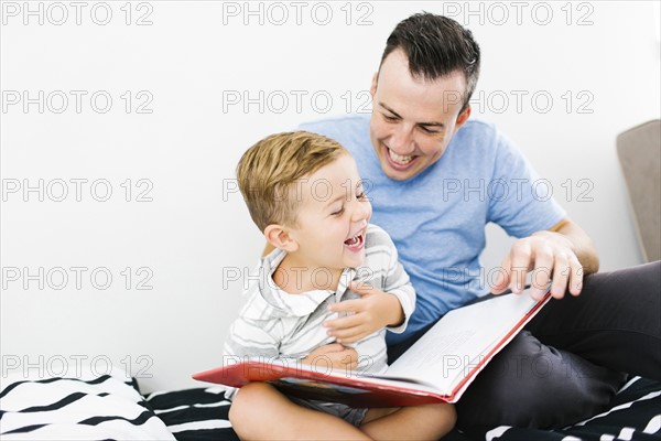 Father and son (4-5) sitting on bed and holding book