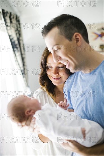 Father carrying daughter (0-1 months) and standing next to mother