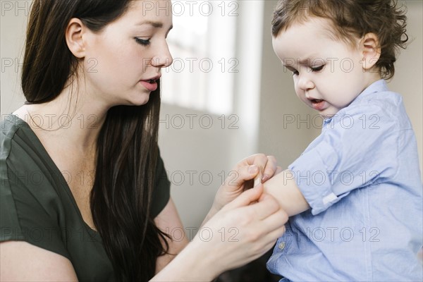 Mother applying plaster on son's (4-5) arm