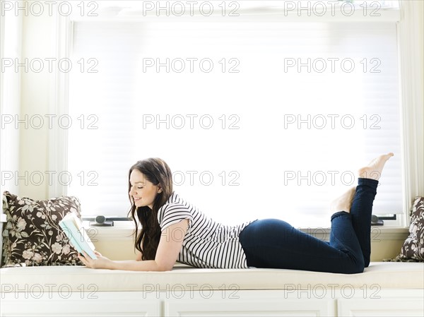 Woman lying on couch and reading book