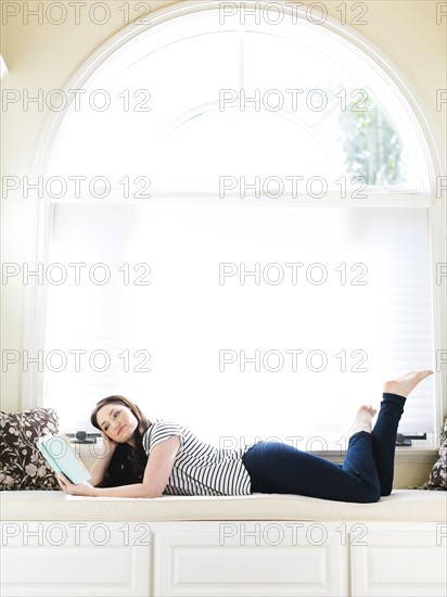 Woman lying on couch and reading book