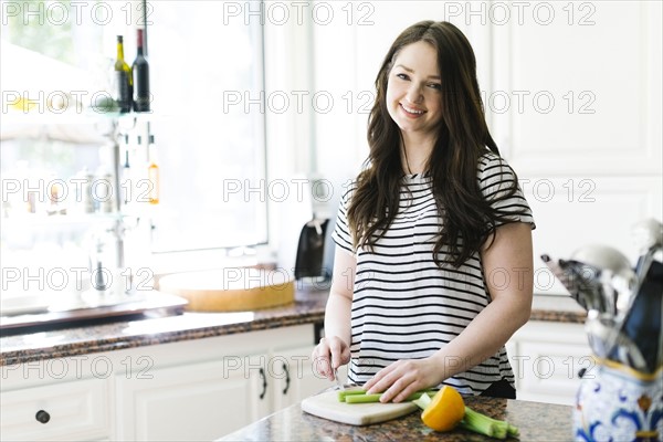 Woman cutting lemon and celery in kitchen