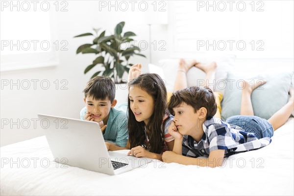 Siblings (10-11, 6-7, 8-9) lying in bed and using computer