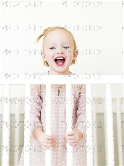 Content small girl ( 12-17 months)  with mouth open standing in crib