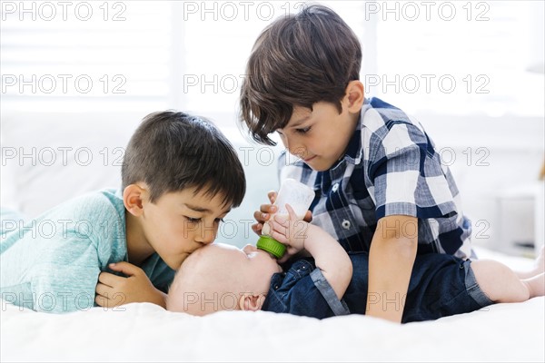 Older brothers( 6-7, 8-9) feeding small brother  (12-17 months) lying on bed