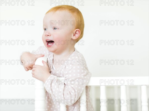 Small girl ( 12-17 months) with red hair standing in crib