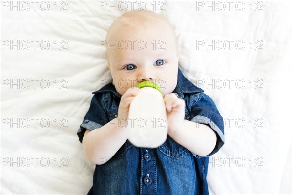 Baby boy (12-17 months) lying on back and drinking milk in bottle