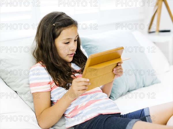 Portrait of content girl  (10-11) reclining on bed and using tablet