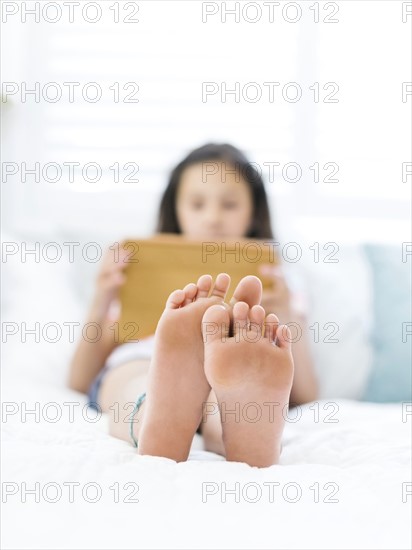 Girl (10-11) lying on back and using tablet with naked feet in foreground