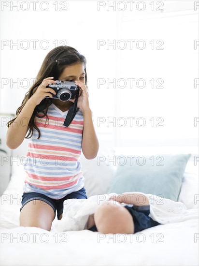 Girl (10-11)  taking photo of her small brother (12-17 months)  lying on bed