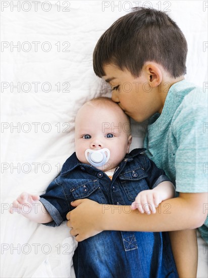 Portrait of boy (8-9) kissing his younger brother (12- 17 months)