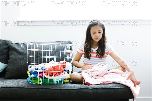 Girl (10-11 ) with laundry sitting on sofa