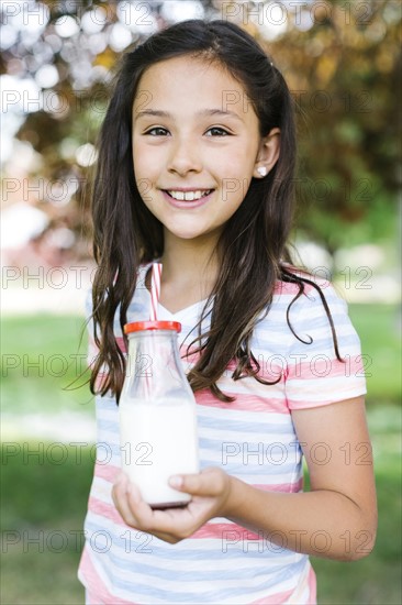 Girl (10-11) in park holding glass of milk with straw