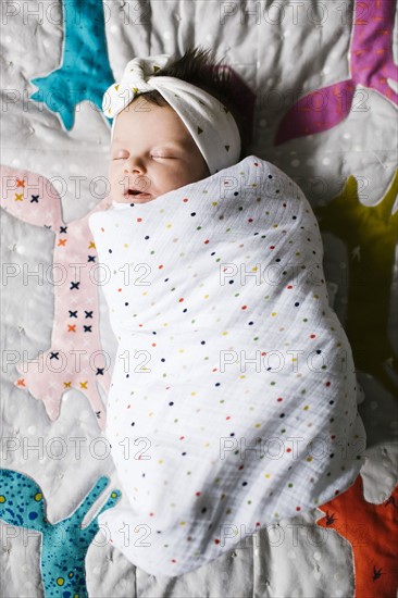 Baby girl (0-1 months) wrapped in blanket sleeping on bed