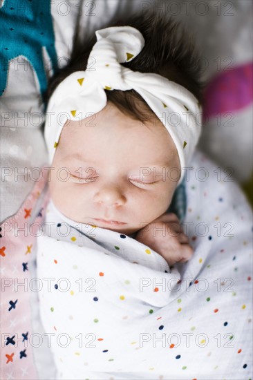 Baby girl (0-1 months) wrapped in blanket sleeping on bed