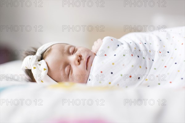 Baby girl (0-1 months) wrapped in blanket sleeping on bed