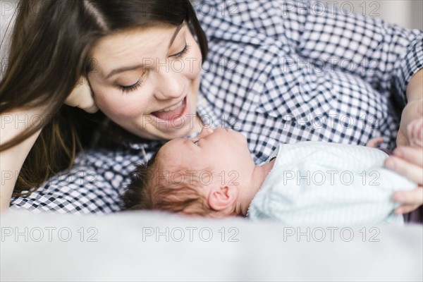 Young mother with baby girl (0-1 months) lying on bed