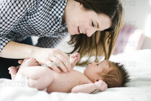 Young mother with baby girl (0-1 months) lying on bed