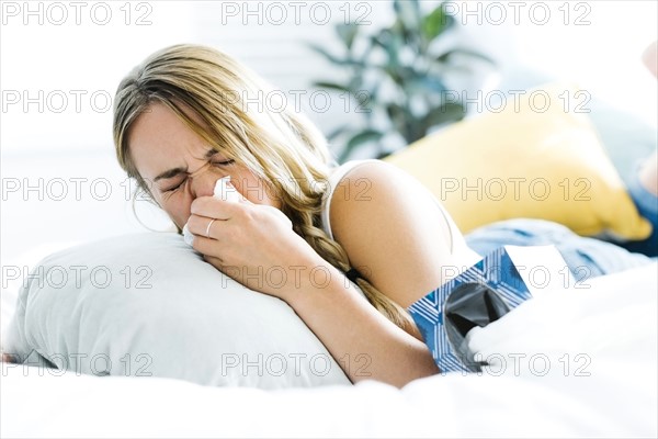 Young woman lying on bed and blowing nose