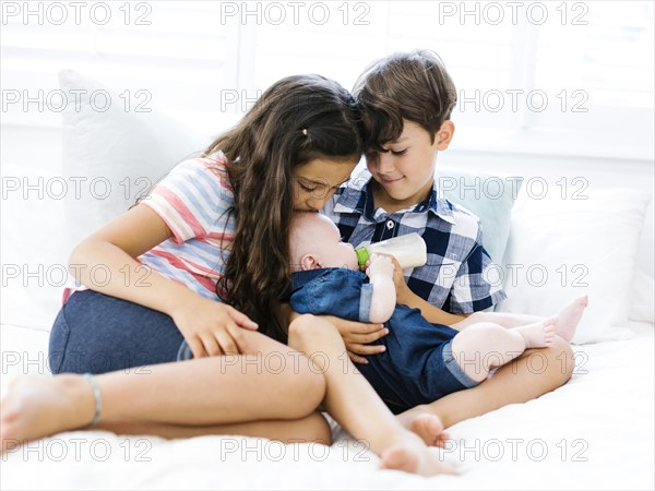 Three siblings (6-11 months, 6-7, 10-11) sitting together on bed