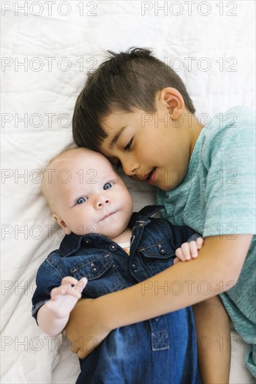 Two brothers (6-11 months)  lying on bed and hugging