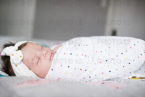 Baby girl (0-1 months) wrapped in blanket sleeping on bed