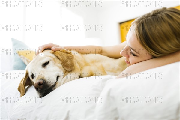 Young woman  stroking golden retriever in bed