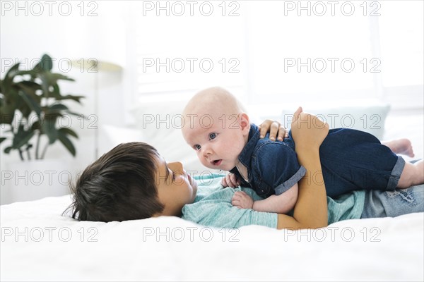 Boy ( 8-9 ) lying on bed and embracing brother ( 2-5 months )