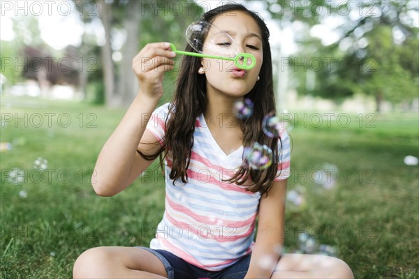 Portrait of girl ( 10-11 ) sitting in meadow and blowing soap bubbles