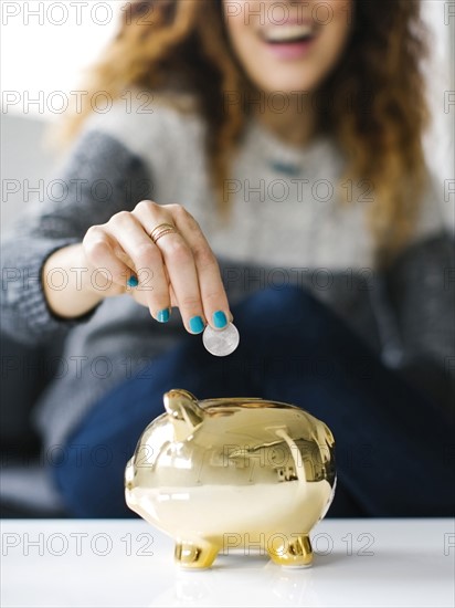 Woman dropping coin into gold piggy bank