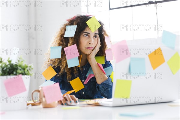 Woman covered with sticky notes using laptop at table