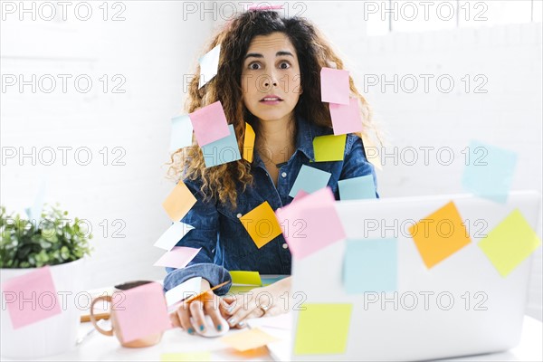 Woman covered with sticky notes using laptop at table