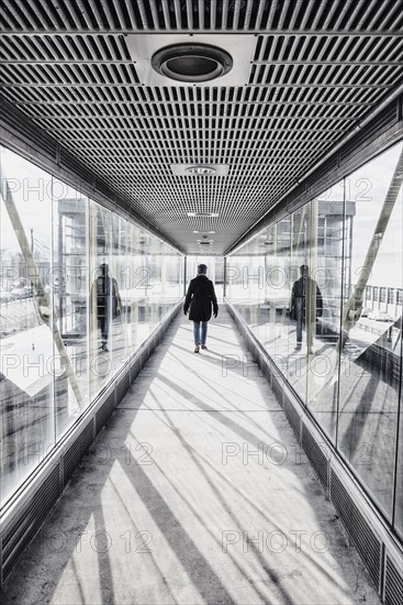 USA, Massachusetts, Boston, Woman walking down glass and metallic walkway at train station