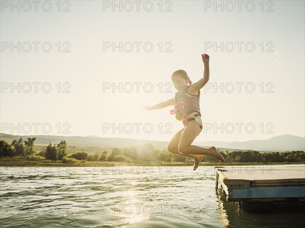 Girl (4-5) jumping into lake from pier