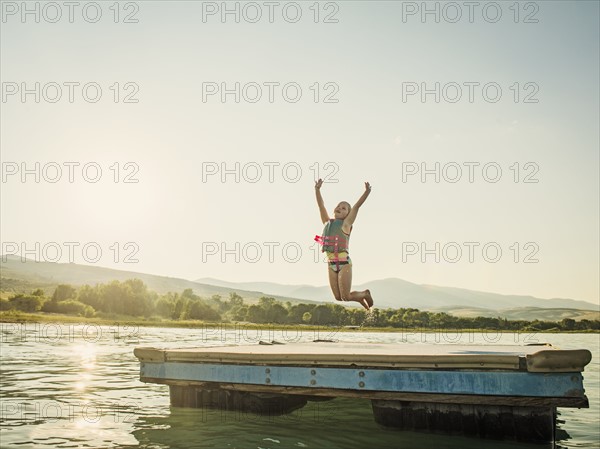 Girl (4-5) jumping into lake from pier