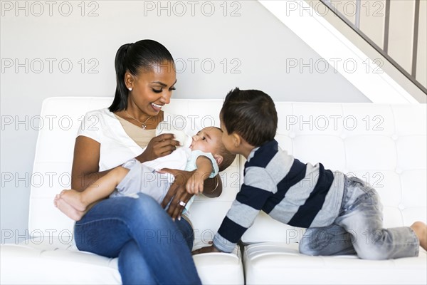 Mother with two sons (2-5 months, 2-3) on sofa