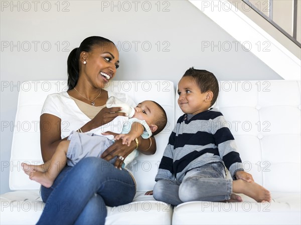 Mother with two sons (2-5 months, 2-3) on sofa