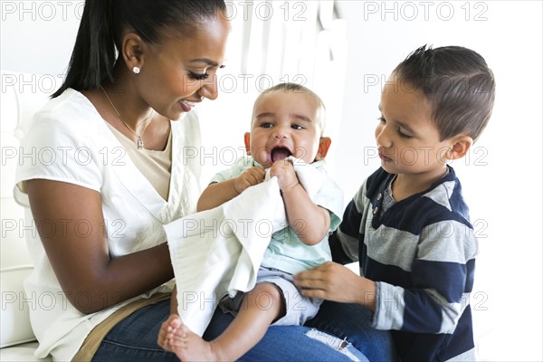 Mother with two sons (2-5 months, 2-3) on sofa