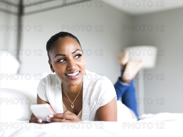 Portrait of woman lying on bed and holding smart phone