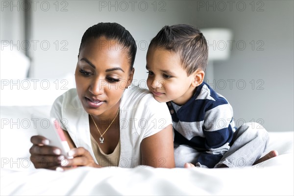 Mother and son (2-3) lying on bed and using smart phone