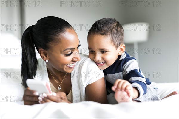 Mother and son (2-3) lying on bed and using smart phone